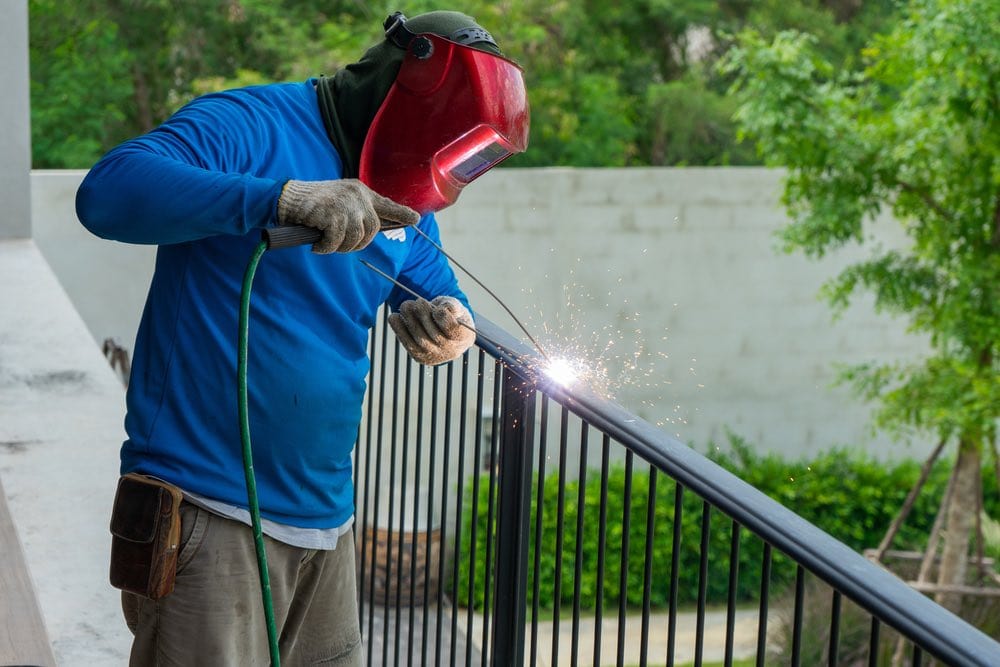 Welding wearing helmet working on fence at home
